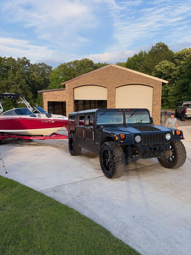 Black Jeep parked in a driveway beside a red-and-white boat, with a brick garage in the background.