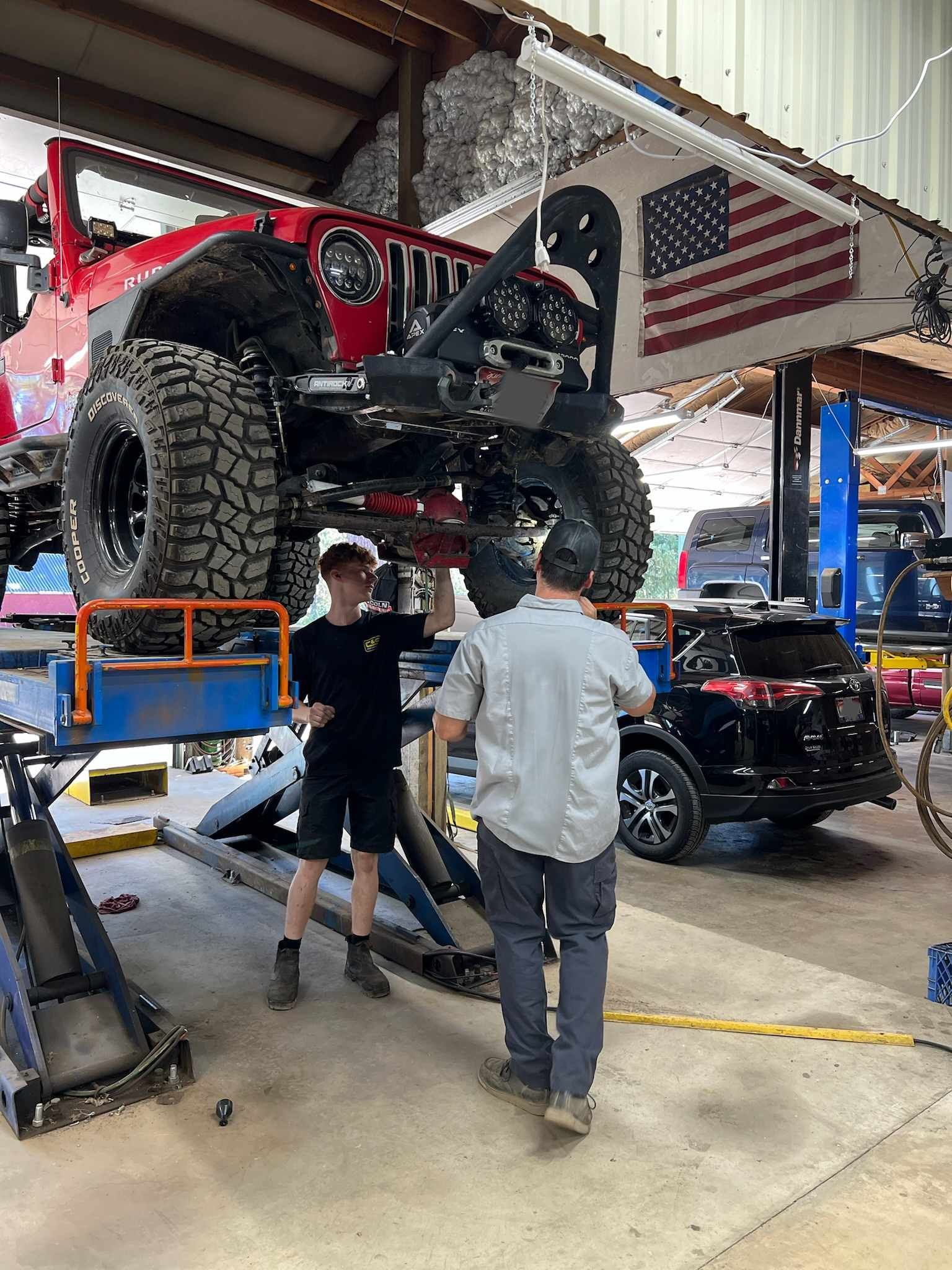 Two men are working on a jeep in a garage.