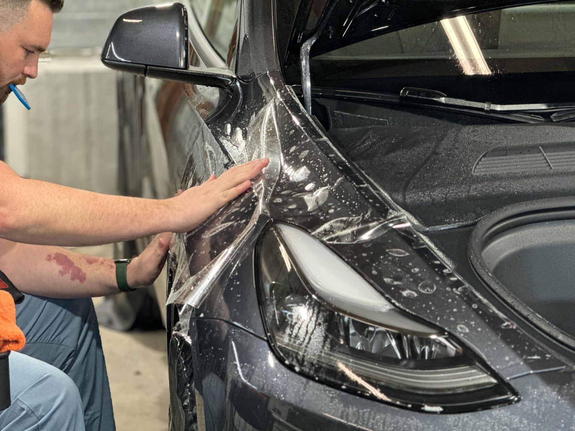 A man is wrapping a tesla model 3 in plastic.