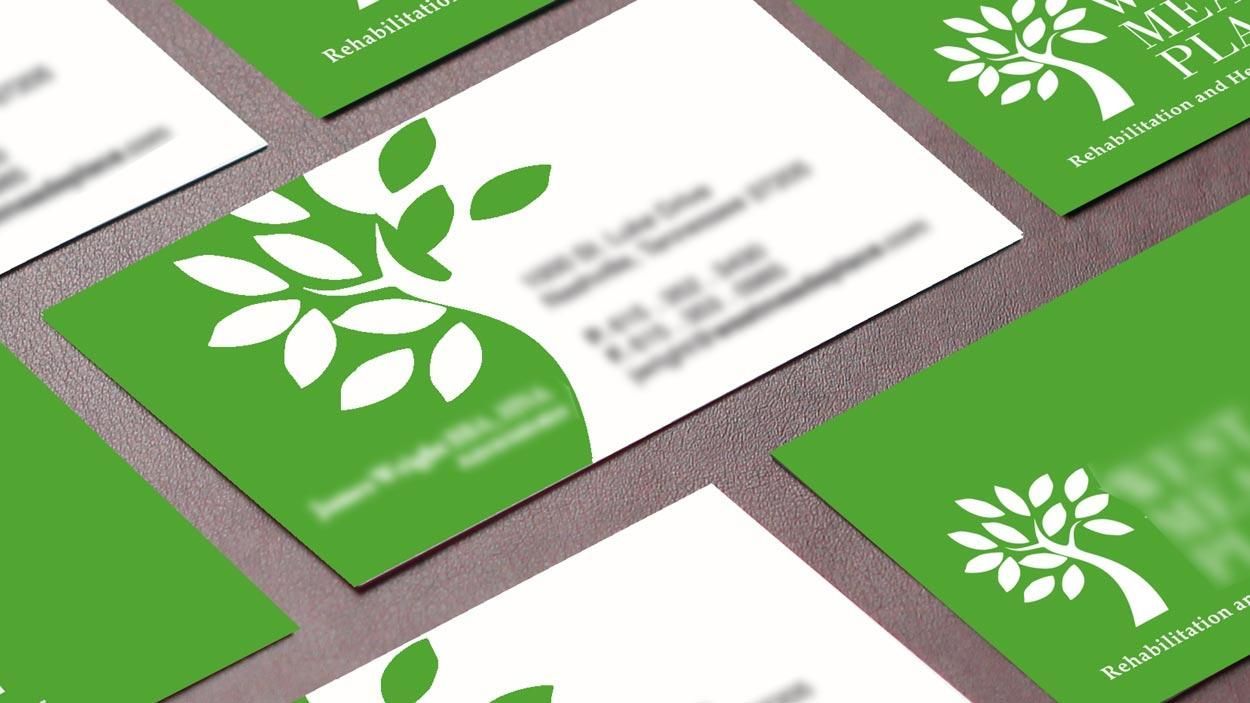 Green-and-white business cards with a leaf logo arranged on a tabletop spread