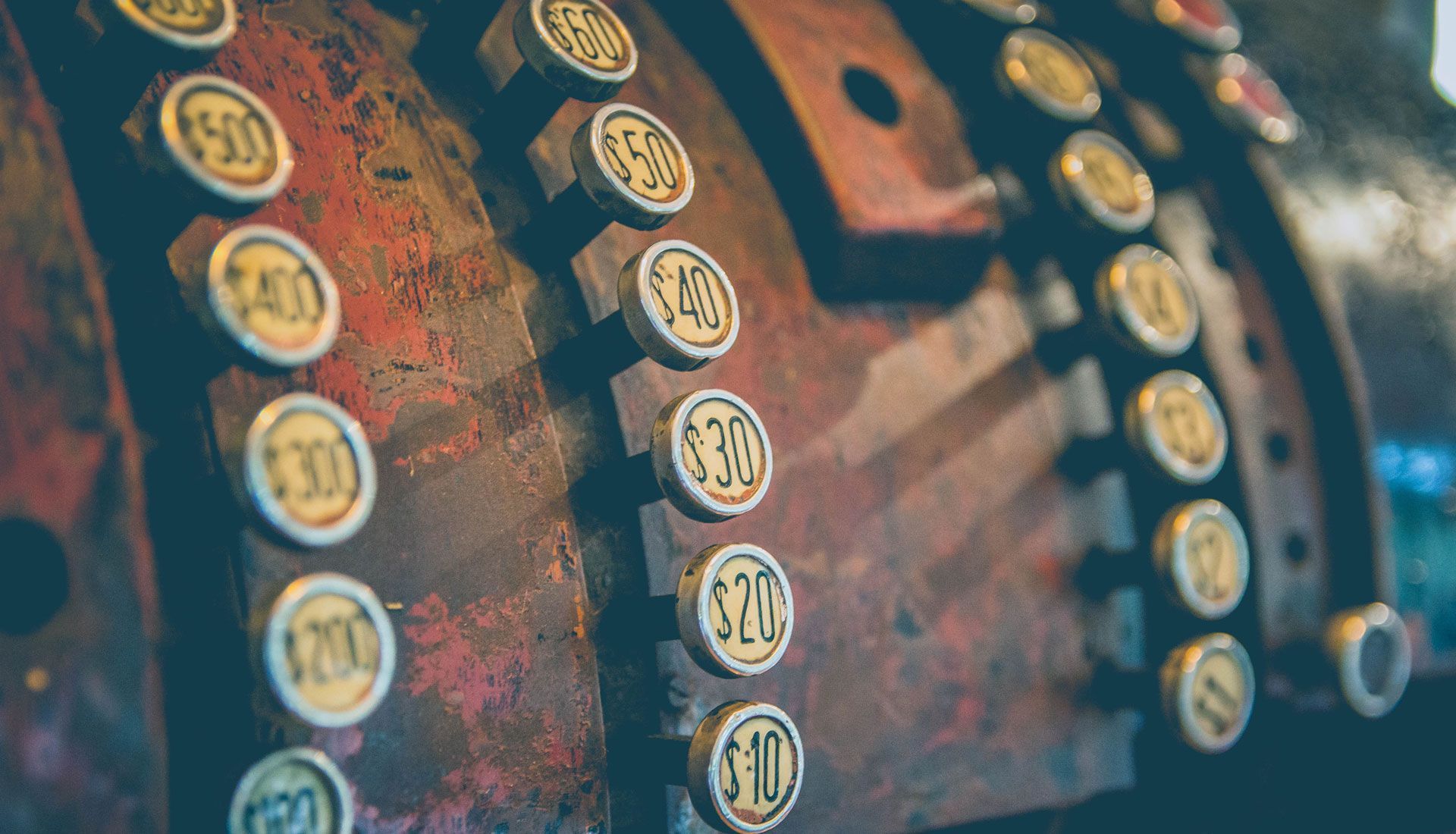 Close-up of a vintage cash register with rows of metal number buttons in warm, blurred light