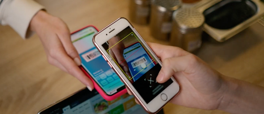 Hands exchanging smartphones with colorful app screens over a wooden table.