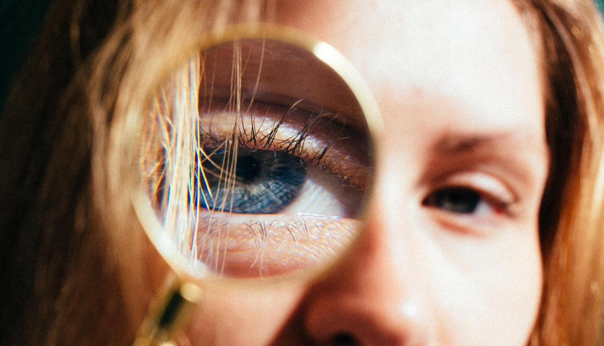 Close-up of a person’s eye with a magnifying glass reflecting blue iris and eyelashes