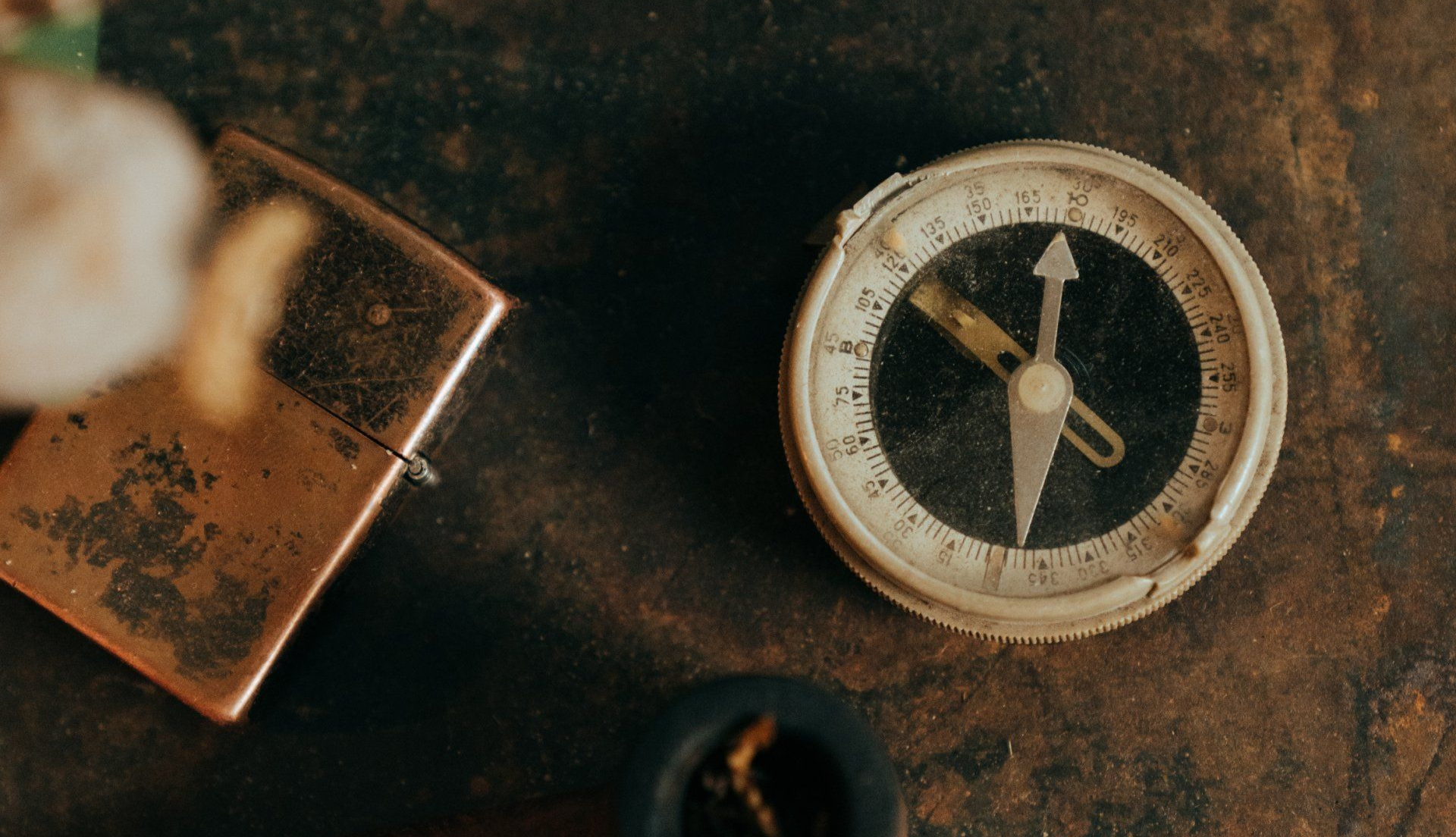 A weathered compass beside a rusty padlock on a dark, textured surface.