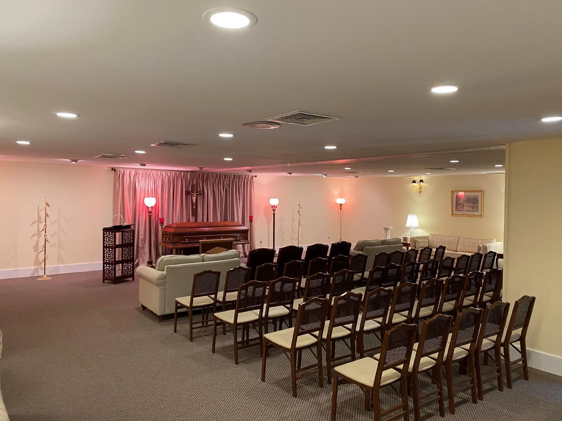 Empty event hall with rows of chairs facing a small stage and white sofa, lit by soft pink and white lights