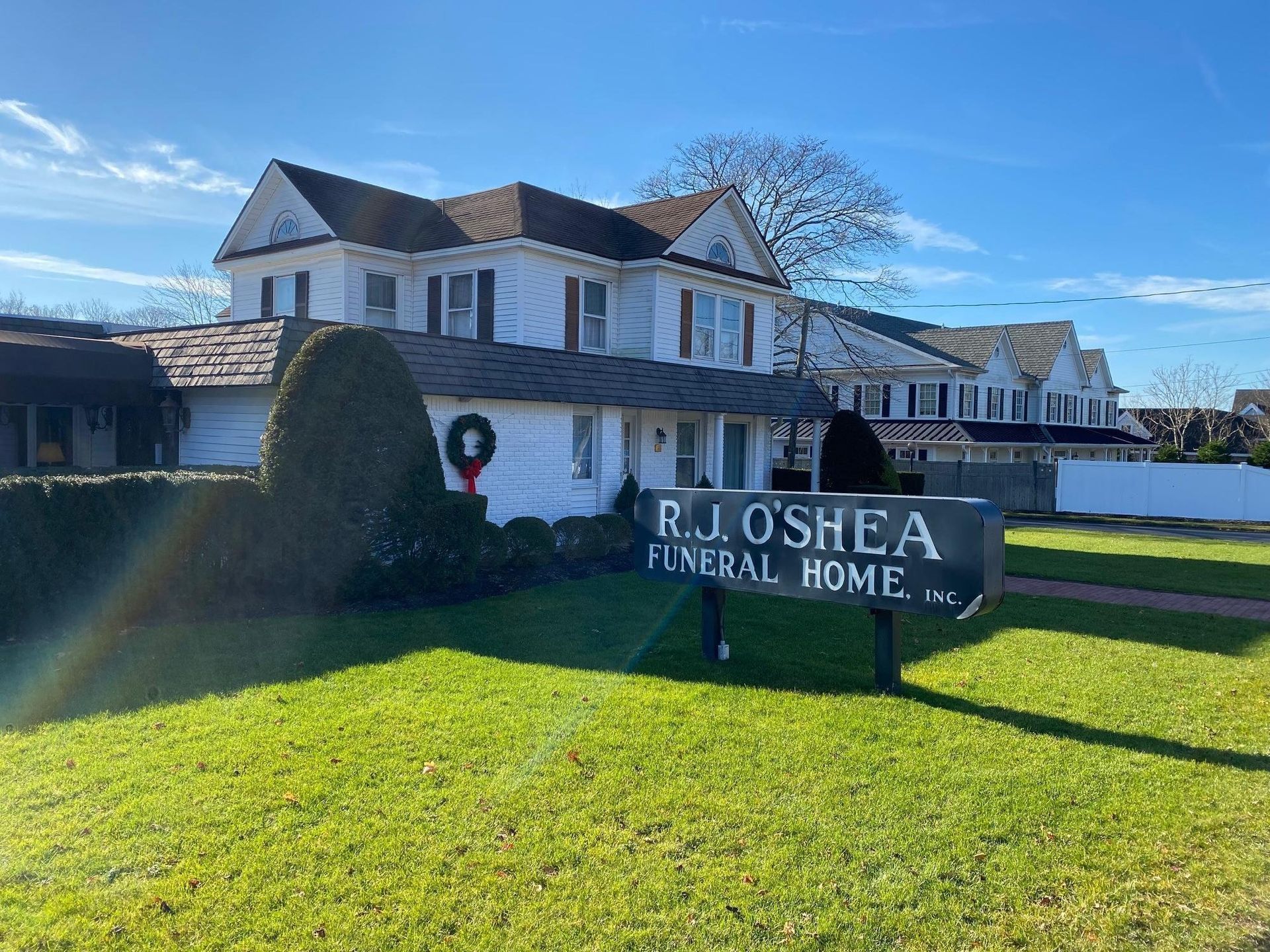 R.J. O'Shea Funeral Home building with sign, white house-style exterior and green lawn under blue sky