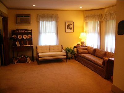 Cozy living room with tan carpet, beige sofa, wooden shelves, lamp, and curtained windows