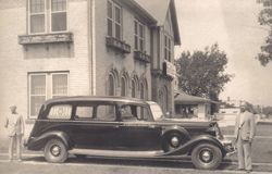 A black and white photo of an old car parked in front of a building.
