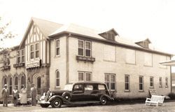 A black and white photo of a car parked in front of a large building.
