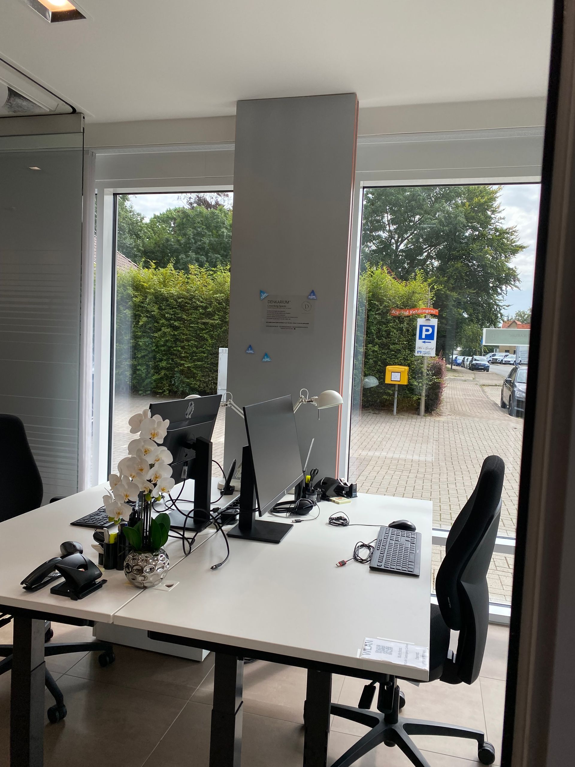 Zwei Schreibtische mit Computern und Stühlen in einem Büro mit einem großen Fenster.