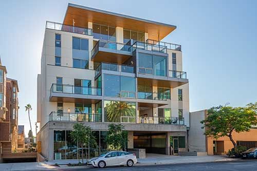 Modern apartment building with glass balconies and a parked car on the street