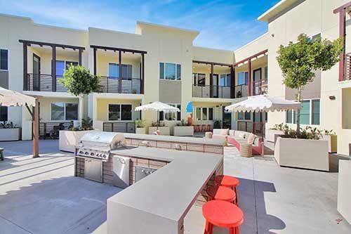 Modern courtyard patio with red stools, white umbrellas, and apartment buildings around a pool area