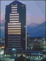 Tall dark office tower at dusk with lit windows against a cloudy evening sky.