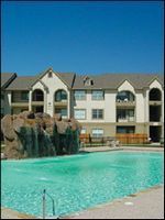 Apartment complex pool with turquoise water and a faux-rock waterfall under a clear blue sky