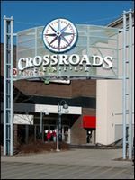 Entrance sign for Crossroads shopping center with a compass logo and glass facade behind it