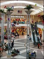 Busy shopping mall atrium with escalators, storefronts, and a large “YONKERS” sign overhead