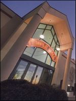 Tilted view of a building entrance with lit glass doors and an arched orange sign at dusk