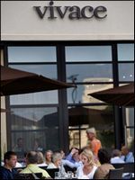 Outdoor café patio with people dining under umbrellas beneath a Vivace sign.