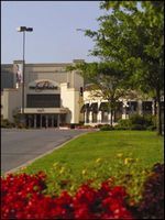 Landscaped building entrance with trees, green lawn, and red flowers in the foreground