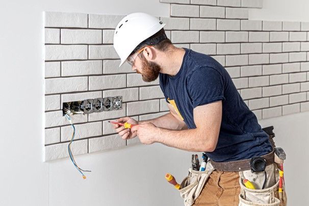 A man is working on an electrical outlet on a brick wall. A man is working on an electrical outlet on a brick wall.