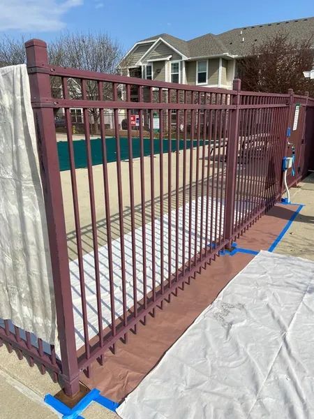 Burgundy metal fence around a pool, masking paper taped to the ground.