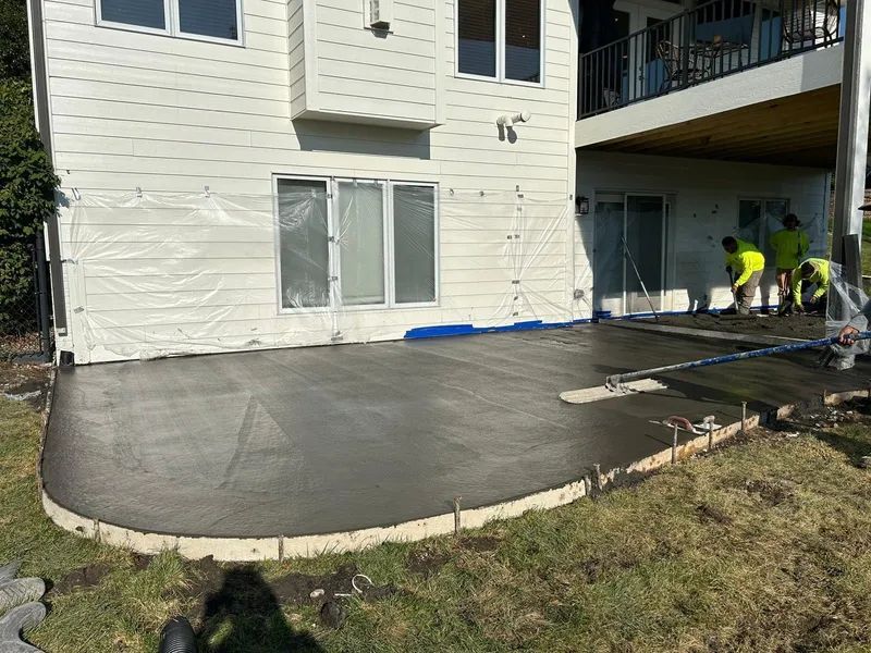 Concrete patio being poured next to a house with workers in the background.
