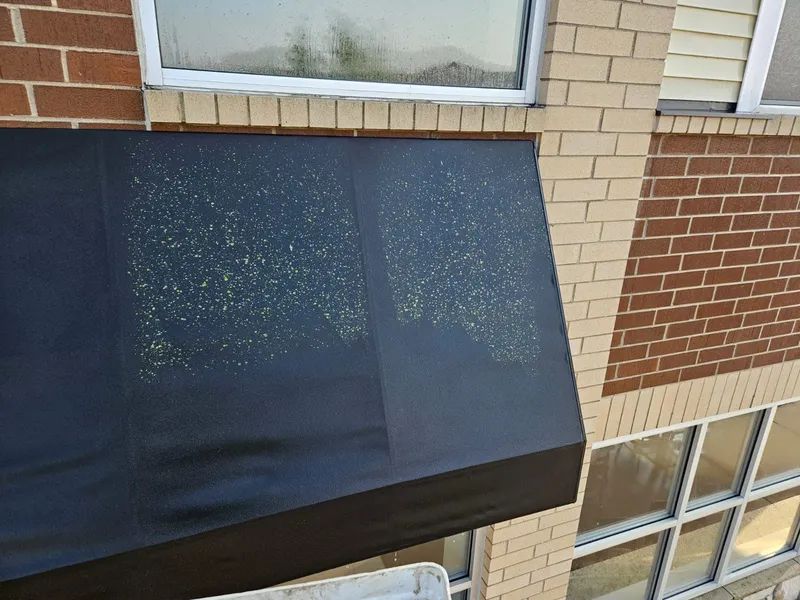 Black awning with yellow spots on brick building below a window.