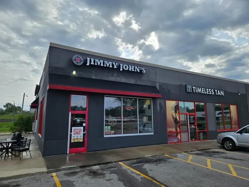 Jimmy John's sandwich shop next to Timeless Tan, gray building with red accents, cloudy sky.