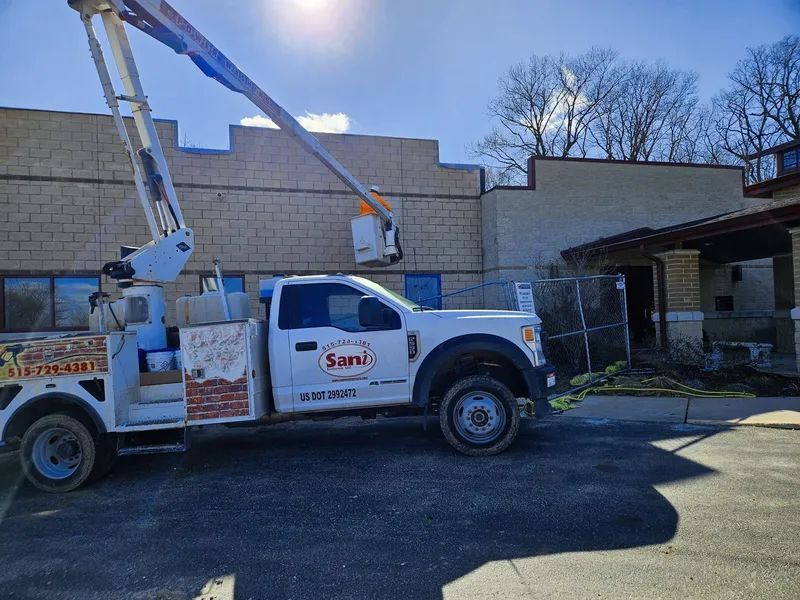 White truck with a crane parked near a building. The crane arm is extended. Sunny day.