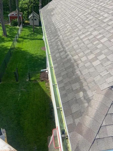 Overhead view of a roof with a gutter filled with debris, near a green lawn.