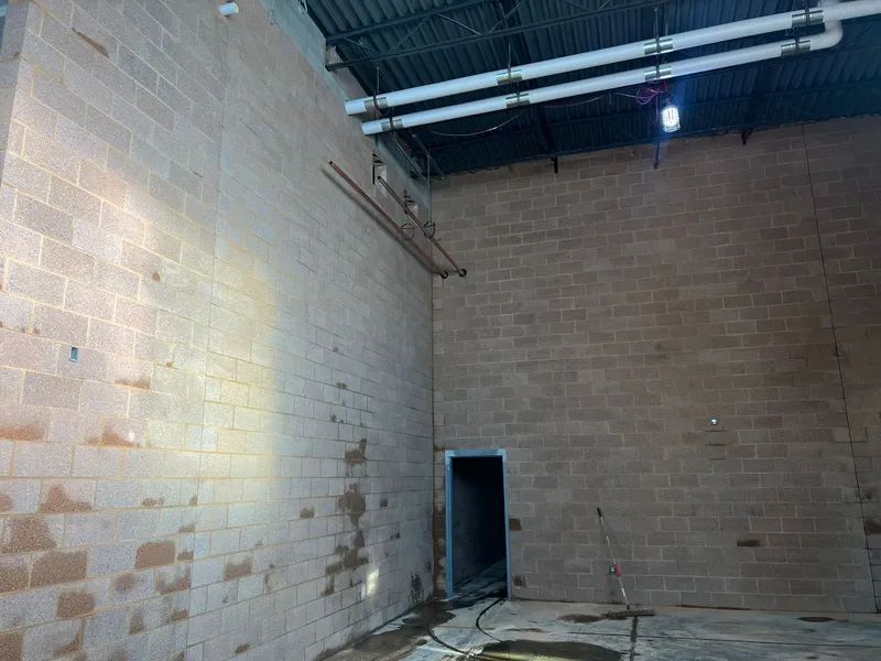 Brick walls inside a building, with a doorway and exposed pipes overhead.