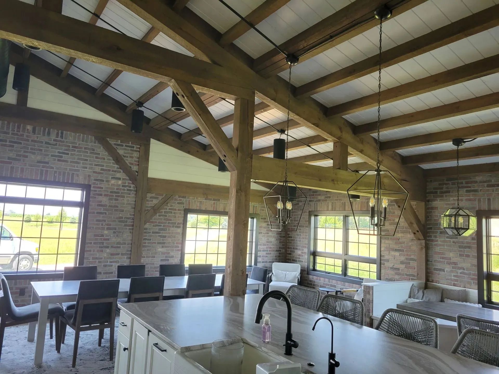 Interior of a barn-style building with exposed wooden beams, stone walls, windows, and dining areas.