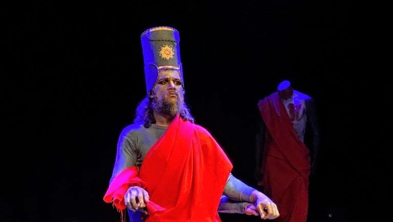 Een man draagt ​​een hoed en een rood gewaad op een podium.