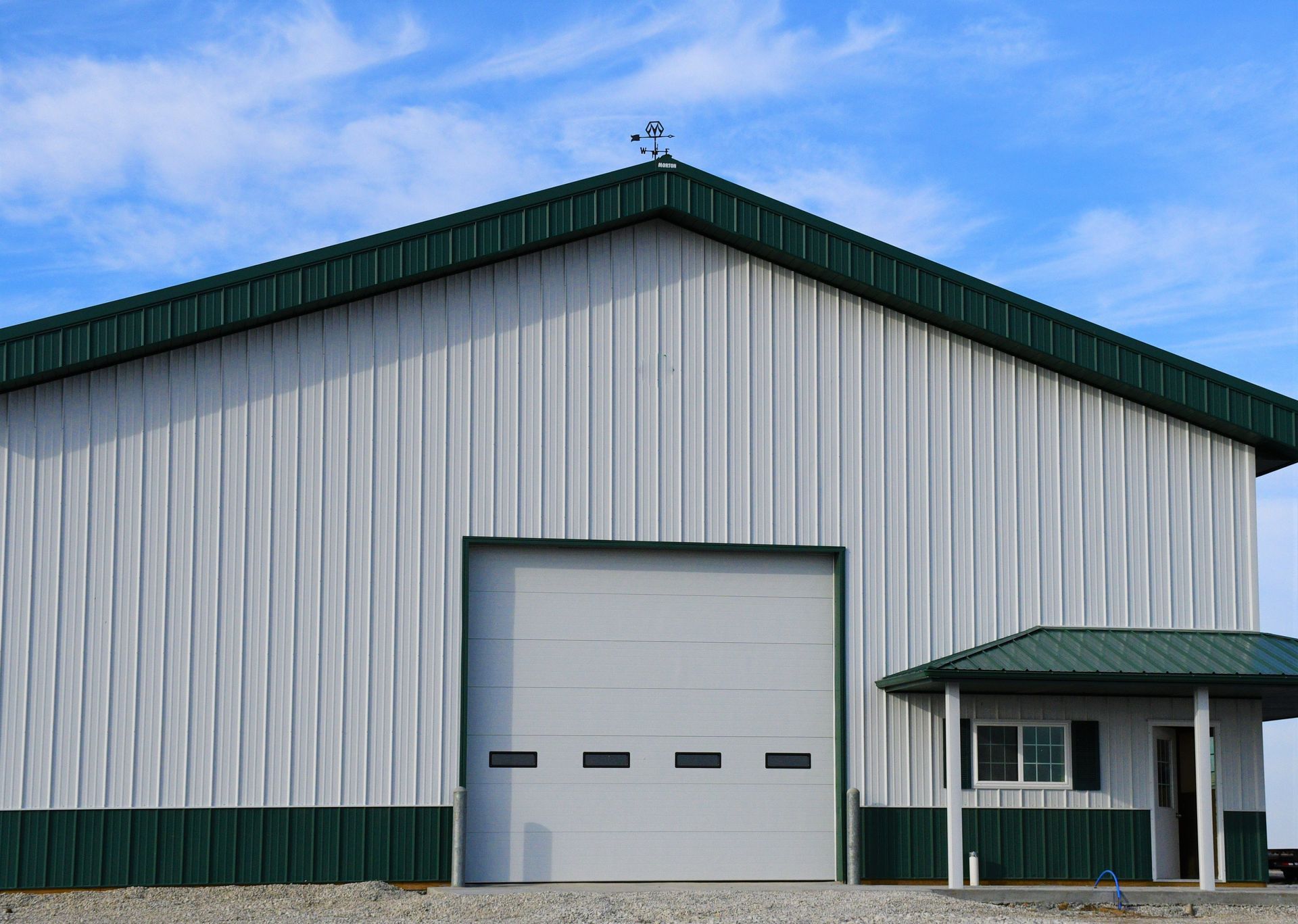 Modern metal barn, green trim, tall garage door, side entry, gravel base.