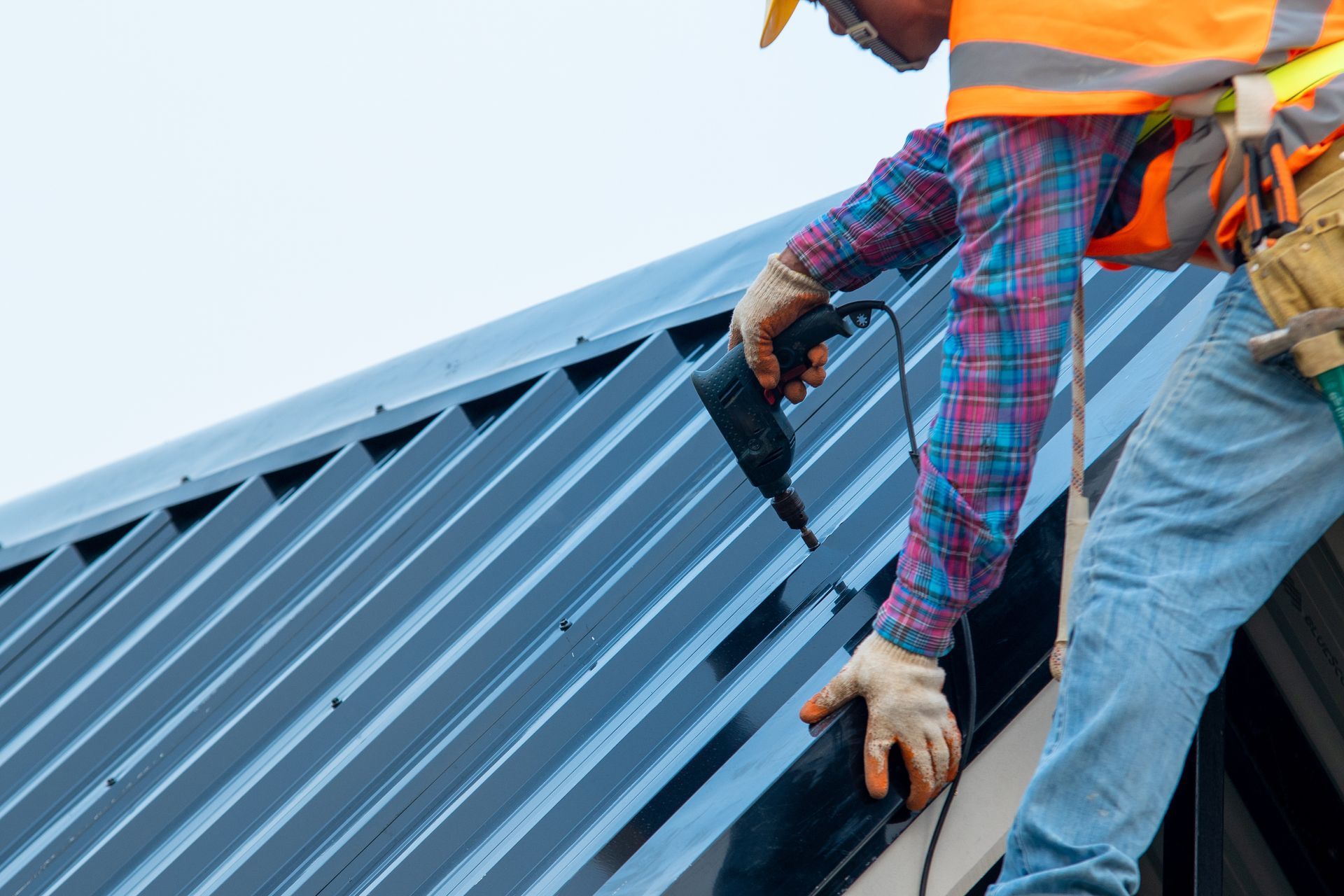 Metal building contractor secured with a safety harness while operating a pneumatic nail gun.