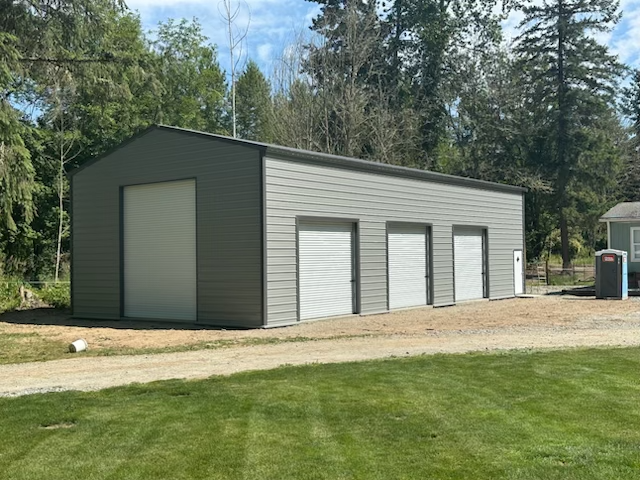 A gray garage with white doors is sitting in the middle of a lush green field.