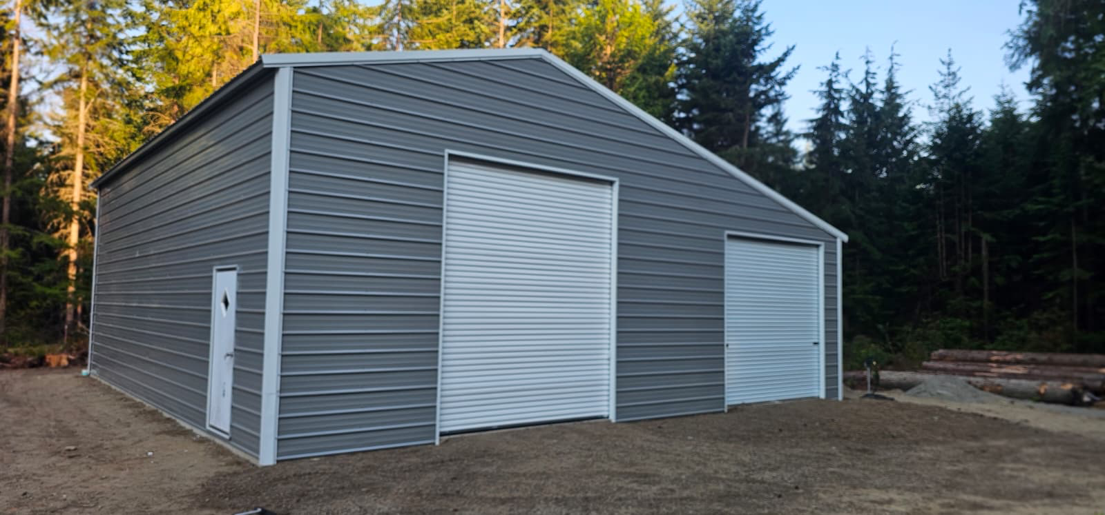 Gray metal shed with white doors in a wooded area.