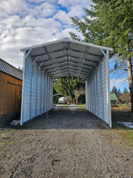 A white carport is sitting in the middle of a gravel driveway.