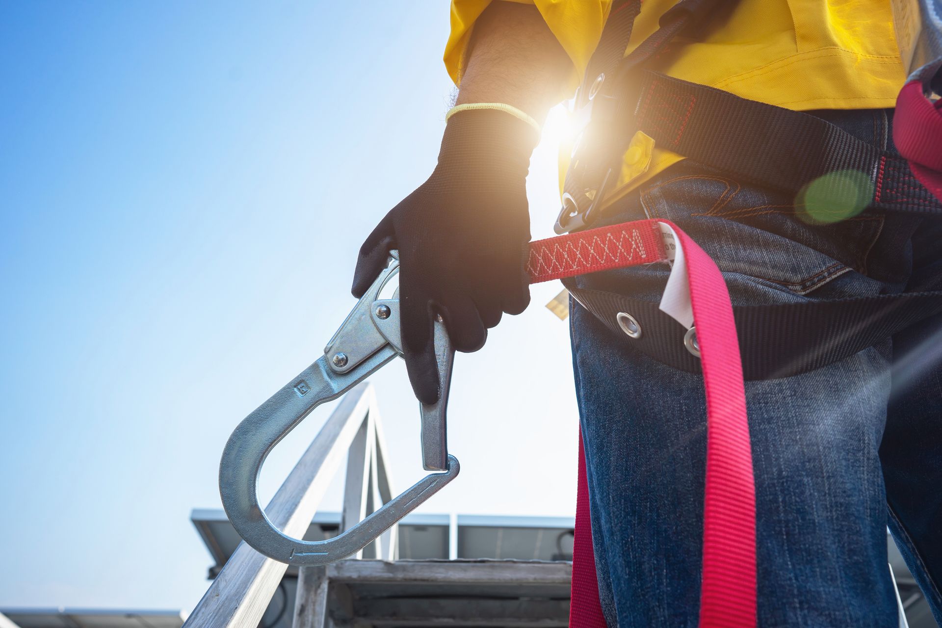 Worker holds safety harness hook with sunlight in background.