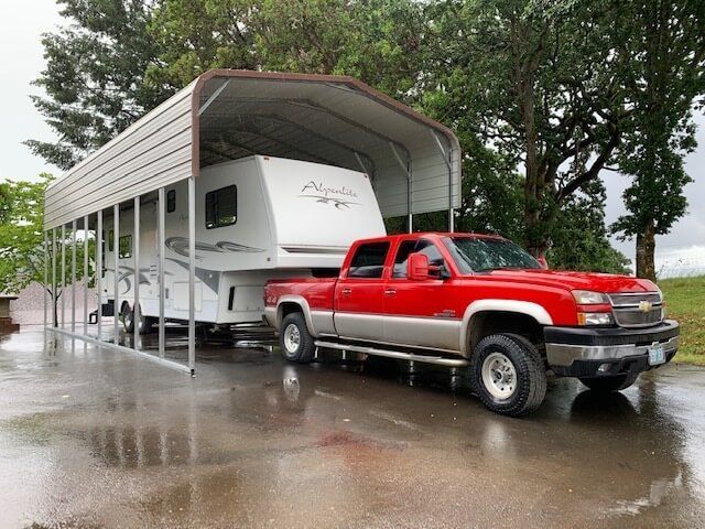 A red truck is parked under a carport with a trailer attached to it.