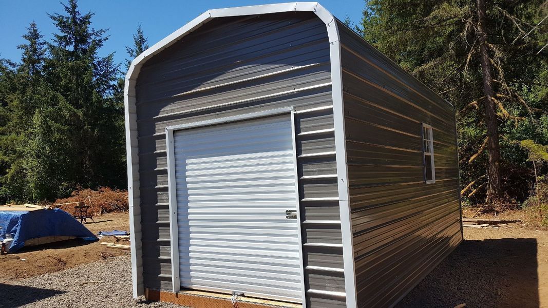 A small metal garage with a white door is sitting in the middle of a dirt field.