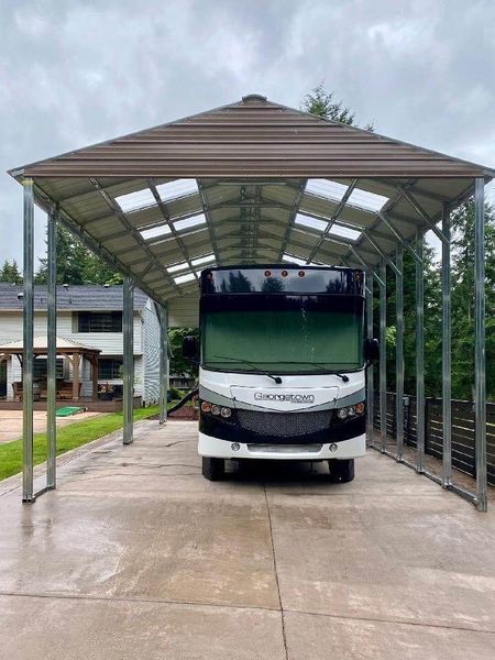 A rv is parked under a carport in a driveway.