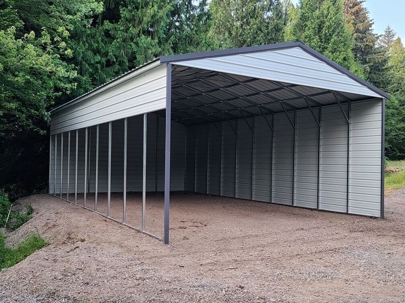 A large metal carport is sitting on top of a gravel road.