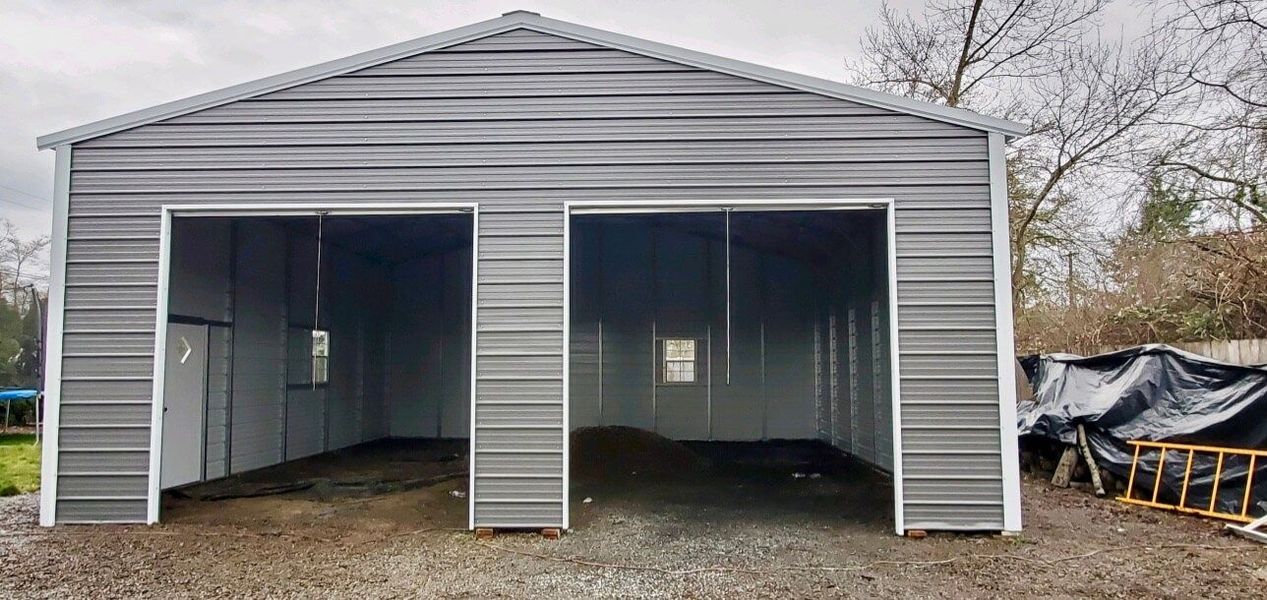 A gray metal garage with two doors is sitting on top of a gravel lot.