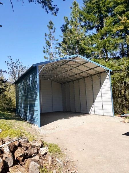 A blue and white metal garage is sitting in the middle of a dirt road.