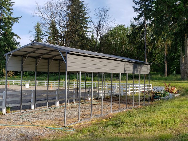 A large metal shed is sitting in the middle of a grassy field.
