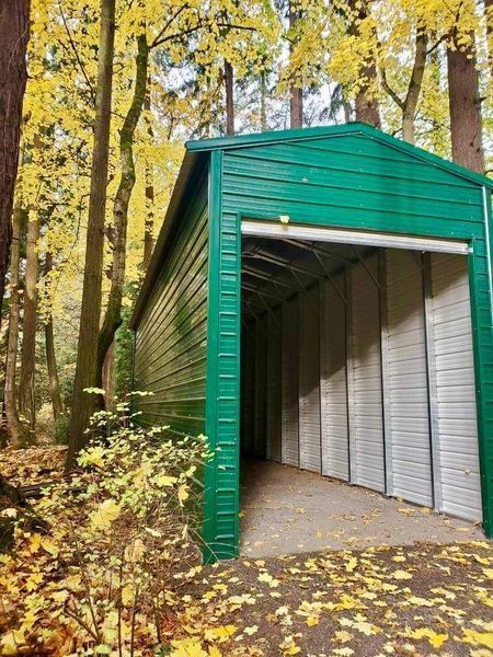 A green and white garage in the middle of a forest.