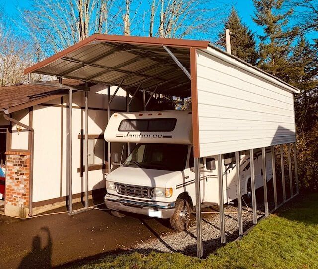 A white RV is parked under a carport.