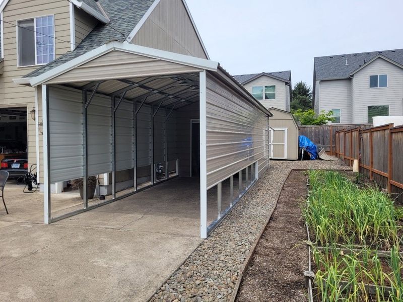 A carport is attached to the side of a house next to a garden.