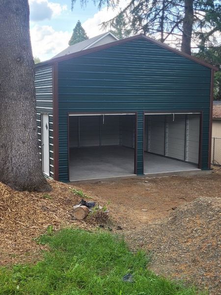A green metal garage with two doors and a tree in the background.